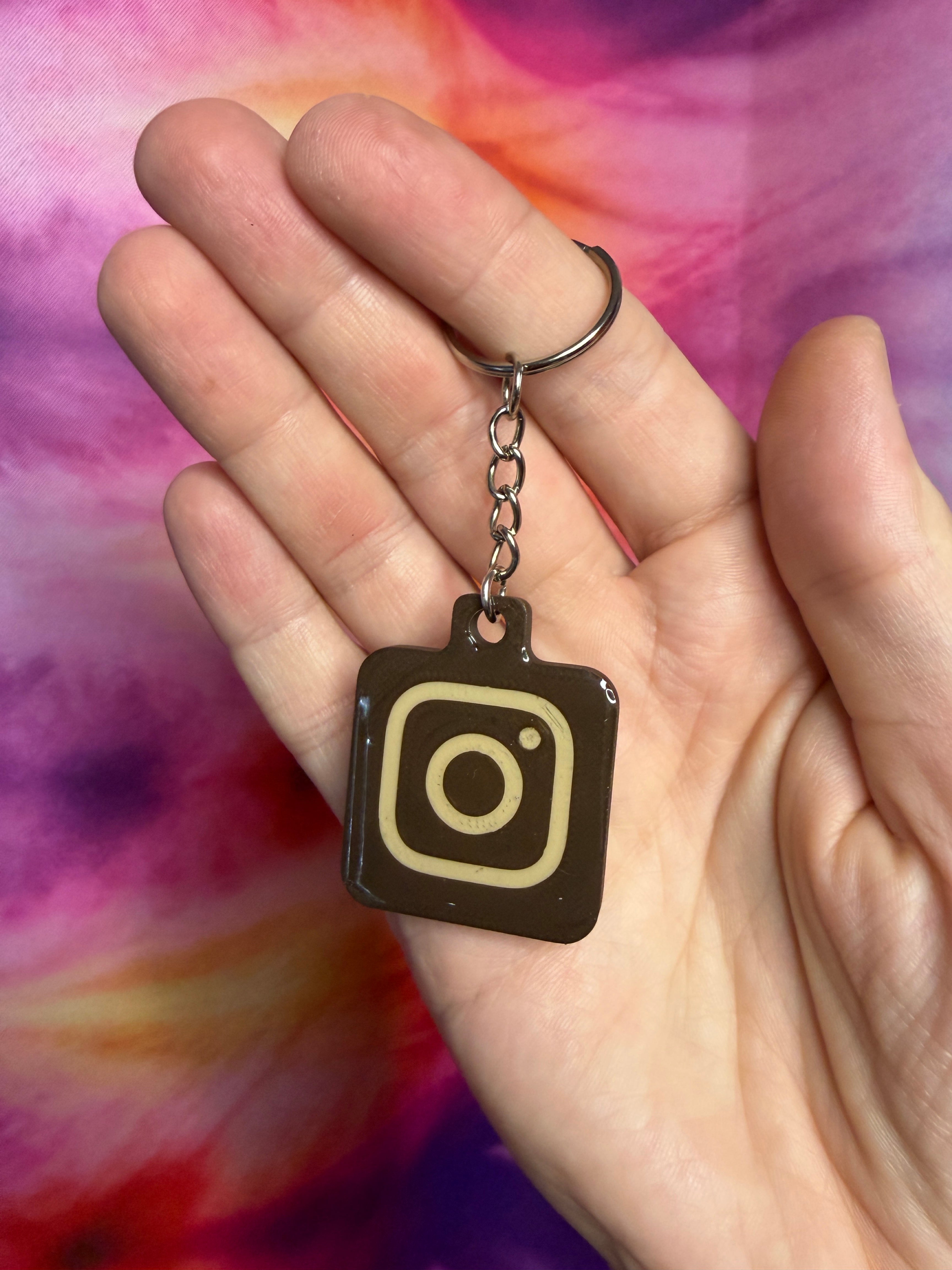 Hand holding a keychain with an Instagram logo chocolate and creme against a tie-dye background
