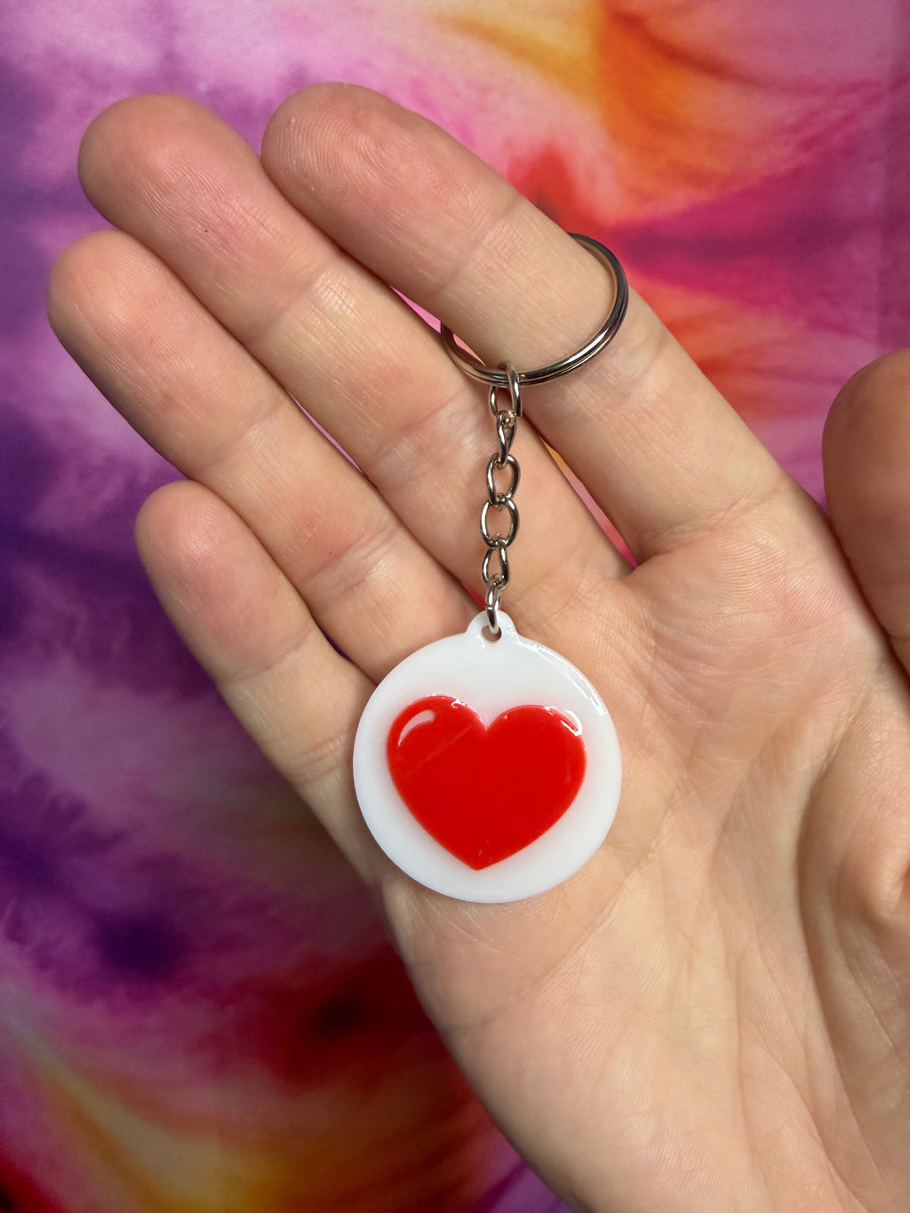 Hand holding a keychain with a red heart design against a colorful background